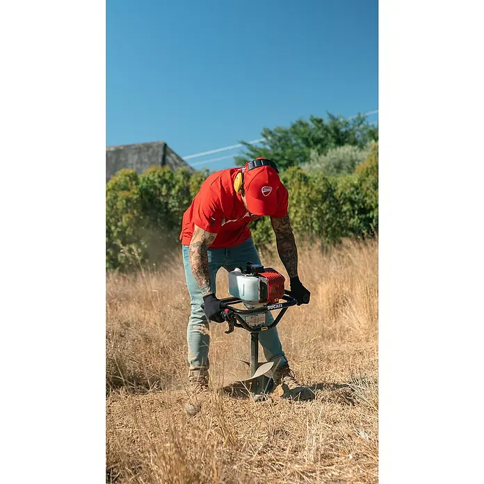 Ahoyadora DEA5200 - 1,3 kW, Anchura de trabajo: 25 cm, 2 tiempos - Un hombre usa una barrena Ducati para cavar un hoyo en la hierba seca mientras usa equipo de protección.