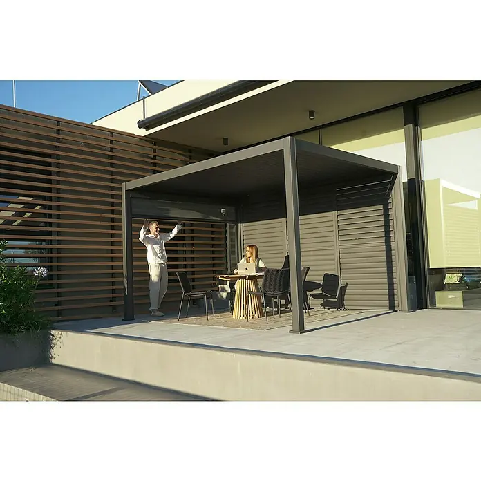 Sunfun Pavillon Korfu - B x T: 400 mm x 300 cm, Farbe Gestell: Anthrazit, Aluminium - Ein Mann öffnet die Lamellen eines modernen grauen Pavillons, unter dem eine Frau an einem Laptop an einem Holztisch sitzt.
