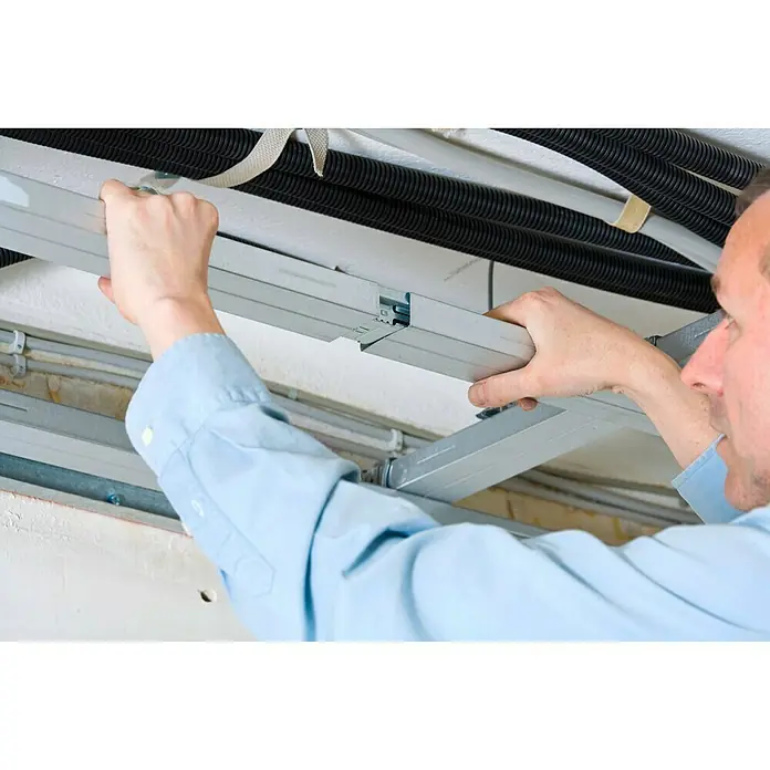 Knauf CD-Multiverbinder - 100 Stk. - Ein Mann installiert eine silberne Deckenkonstruktion mit schwarzen Kabeln im Hintergrund, was auf eine professionelle Installation hinweist.