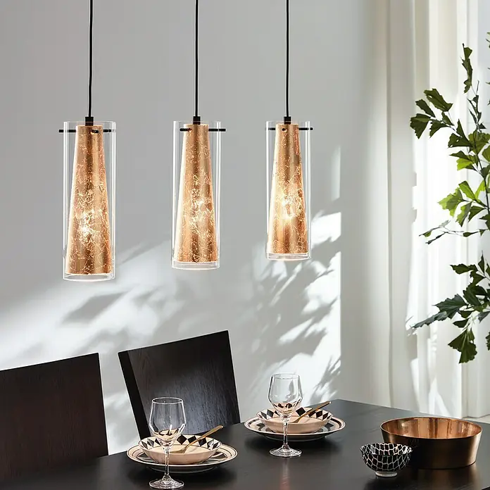 Eglo Pinto Gold Pendelleuchte - Höhe: 110 cm, Max. Systemleistung: 180 W - Ein elegantes Interieur mit drei Pendelleuchten, die ein warmes Licht über einem gedeckten Esstisch verbreiten, wodurch eine einladende Atmosphäre entsteht.