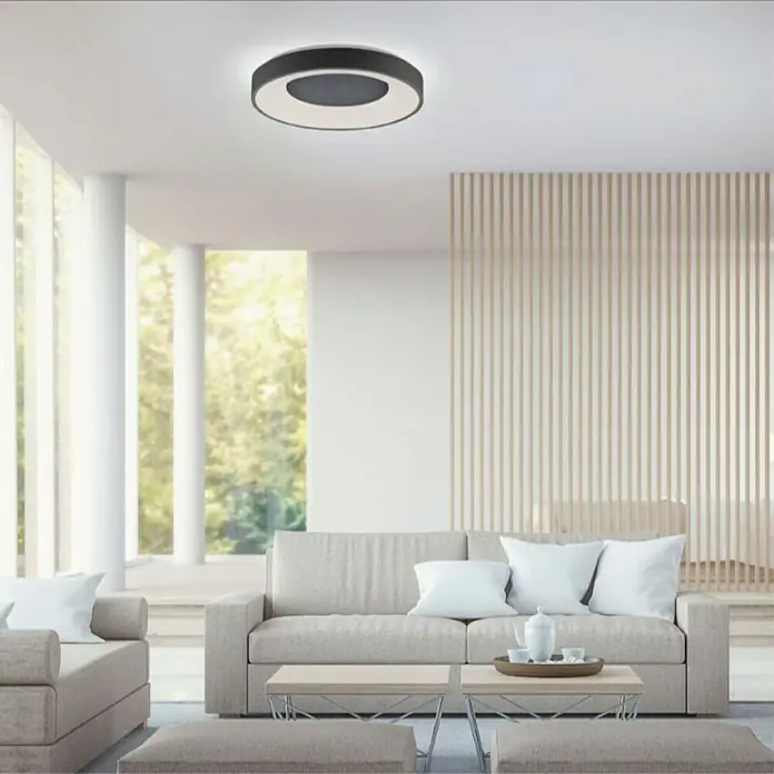 LeuchtenDirekt LED stropna svjetiljka Anika - 60 W, Crne boje, Topla bijela - Moderna stropna svjetiljka s crnim rubom i bijelim svjetlosnim prstenom, koja visi iznad minimalističkog prostora za sjedenje.