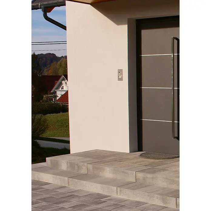 Seesteiner Blockstufe Piazza - 100 x 35 x 15 cm, Anthrazit, Beton - Nahaufnahme einer modernen Haustür mit grauer Tür und silbernen Akzenten, eingebettet in eine helle Fassade mit Treppenaufgang.