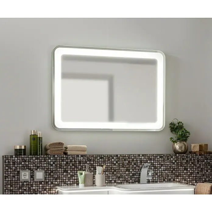 Camargue Stella LED-Lichtspiegel - 100 x 70 cm, Mit Kippschalter, Mit abgerundeten Kanten - Ein beleuchteter Badezimmerspiegel hängt über einem Waschbecken, das mit Pflegeprodukten und Handtüchern dekoriert ist.