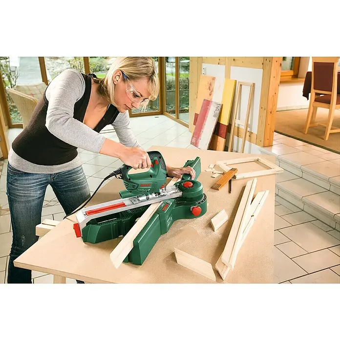 Bosch Stichsäge PST 700 E - 500 W, 500 Hübe/min - 3.100 Hübe/min - Eine Frau arbeitet mit einer Bosch Stichsäge an einem Holztisch, um Holz für einen Rahmen zuzuschneiden. Sie trägt dabei eine Schutzbrille.