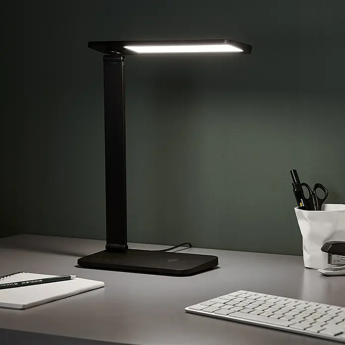 LED-Tischleuchte Seamont - 9 W, L x B x H: 31 x 12 x 37,4 cm, Schwarz - Elegante, moderne schwarze LED-Schreibtischleuchte mit kabelloser Ladefunktion auf einem Schreibtisch mit Büromaterial.