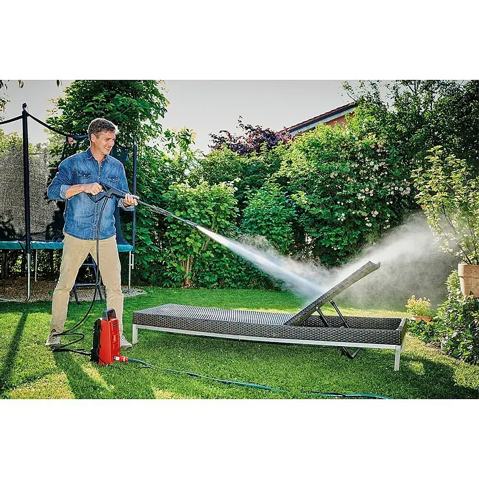 Einhell Classic Hidrolimpiadora de alta presión TC-HP90 - 1.200 W, Presión máx.: 90 bar, Capacidad de bombeo: 372 l/h - Un hombre está limpiando una tumbona de jardín al aire libre con una hidrolimpiadora, con la limpiadora en primer plano.