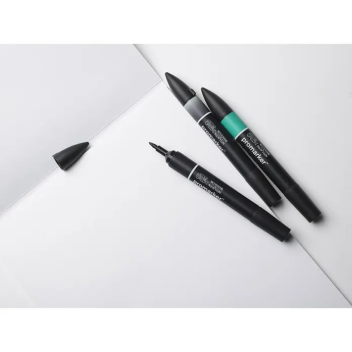 Winsor & Newton Zeichenpapier Marker Block - DIN A4, 75 g/m², Anzahl Blätter: 50 Stk. - Drei Winsor & Newton ProMarker Stifte in Grau, Grün und Schwarz liegen auf einem weißen Untergrund. Ein Stift ist geöffnet.