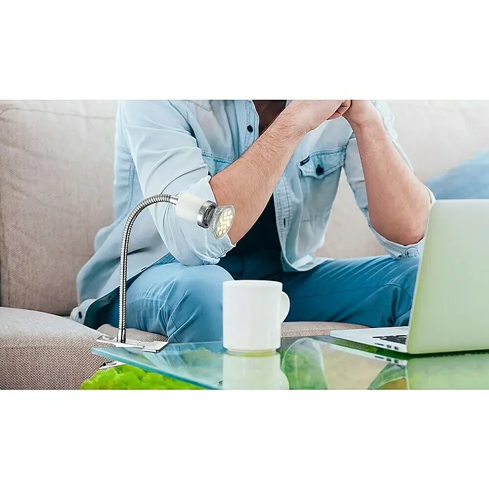 Globo LED-Klemmleuchte Fina - 1-flammig, 3 W, Chrom - Eine flexible LED-Klemmlampe, die auf einem Tisch befestigt ist, scheint auf einen Laptop, während eine Person auf einem Sofa sitzt.