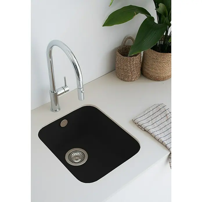 Poalgi Fregadero encastrable Gandía Soft 35 - 44,5 x 38 cm, Gelcoat, Negro - Primer plano de un fregadero de cocina negro con un grifo cromado, complementado con encimeras blancas, plantas en macetas y una toalla a rayas.