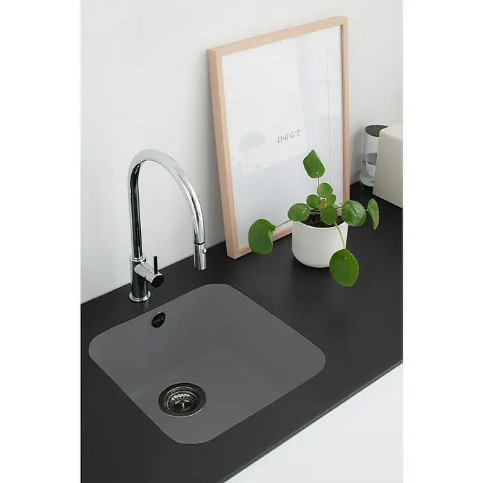 Poalgi Fregadero encastrable Gandía Soft 40 - 44,5 x 44 cm, Gelcoat, Gris - Un fregadero de cocina moderno con un grifo brillante, enmarcado por una planta de interior y una imagen minimalista sobre una encimera oscura.