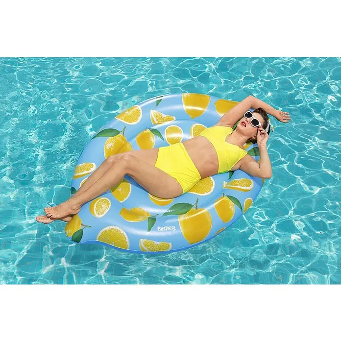 Zračni madrac na napuhavanje Lemon - 122 x 176 cm - Žena se opušta na žutom plovku od limuna u bazenu, noseći bijele sunčane naočale i žuti kupaći kostim, savršeno za sunčan dan.