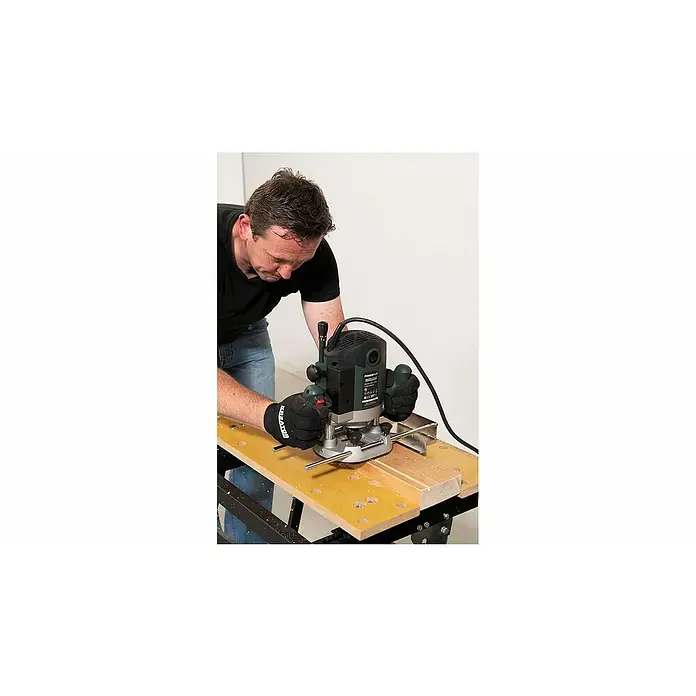 PowerPlus Fresadora de superficie POWP6050 - 2.100 W, Carrera máx. de fresado: 60 mm - Un hombre está trabajando con una fresadora de madera en una pieza de madera. La fresadora es el elemento central de la imagen.