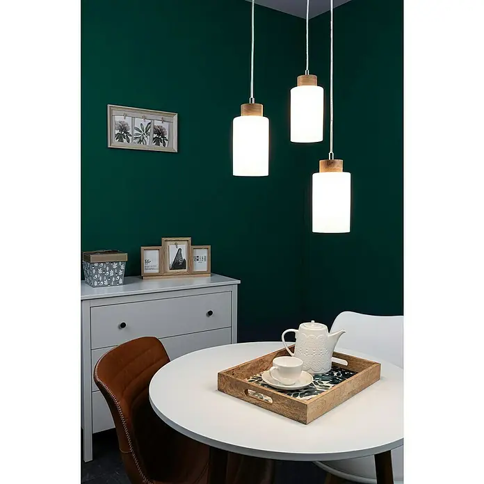 Spotlight Pendelleuchte rund Bosco - 60 W, Ø x H: 300 mm x 110 cm, Weiß, Geölte Eiche, E27 - Elegante Trio-Hängeleuchte mit Holz- und Glasdetails über einem stilvollen Esstisch mit Teegeschirr vor einer satten grünen Wand.