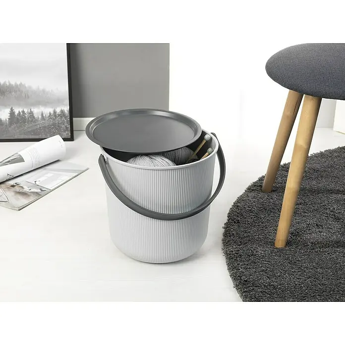 Eimer Akita - L x B x H: 480 x 446 x 445 mm, 53 l, Grau - Ein grauer Strickkorb mit Deckel, gefüllt mit Wolle und Stricknadeln, steht neben einem grauen Hocker auf einem grauen Teppich.
