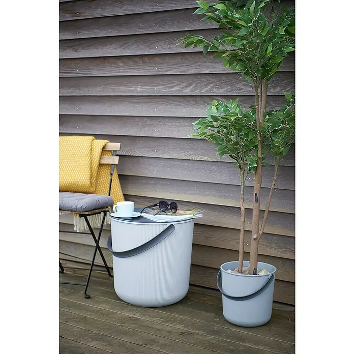 Eimer Akita - L x B x H: 277 x 271 x 258 mm, 10 l, Grau - Ein moderner grauer Outdoor-Hocker dient als Beistelltisch, dekoriert mit Tasse, Sonnenbrille und Magazin, neben einem passenden Pflanzgefäß.