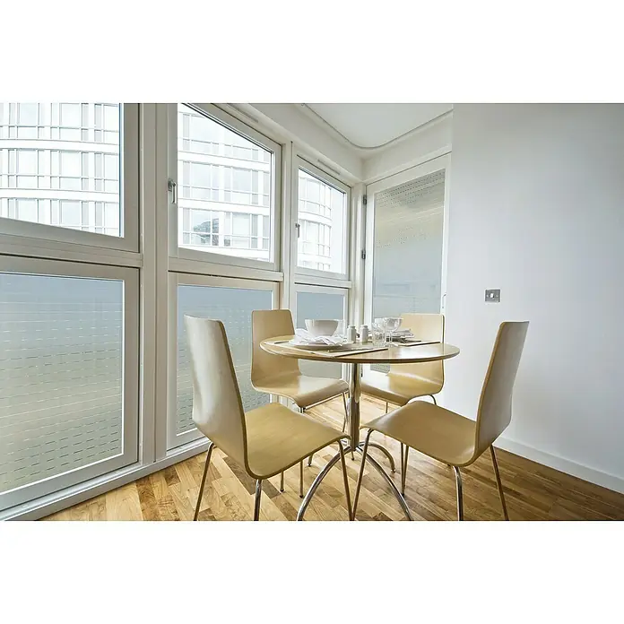 Lámina adhesiva Mayo - Transparente, 150 x 45 cm, Con adherencia estática - Comedor luminoso con mesa de madera, cuatro sillas y grandes ventanas con vistas a un edificio de oficinas.