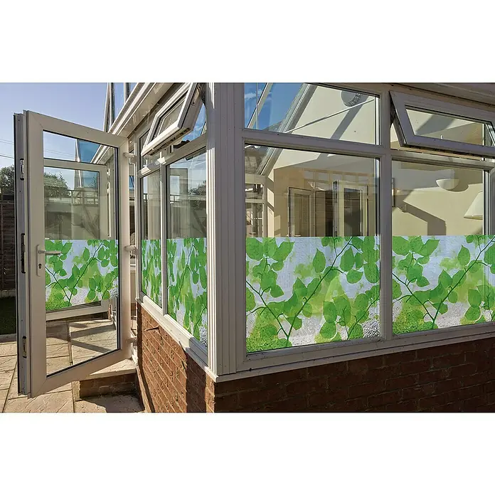 Lámina adhesiva GLS-4654 - Verde/blanco, Con adherencia estática - Primer plano de una lámina para ventanas con diseño de hojas verdes en una ventana de un invernadero, que proporciona privacidad y permite el paso de luz.