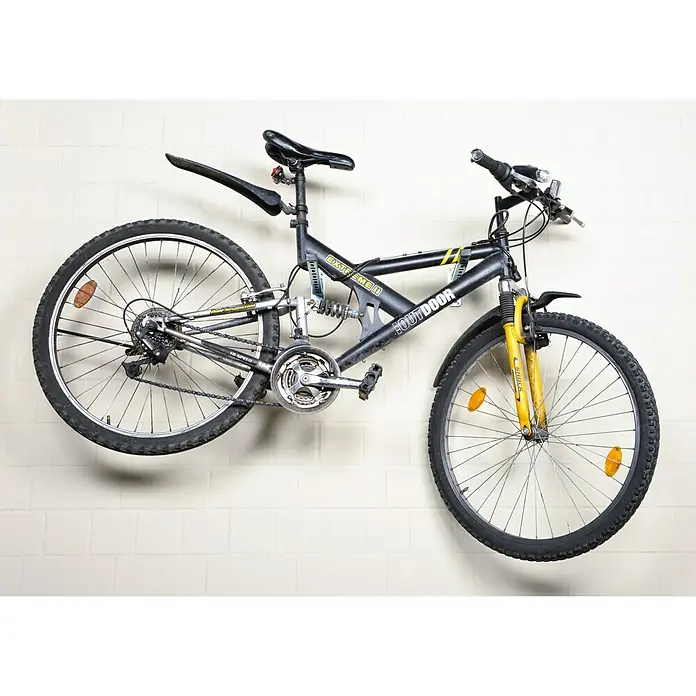 UBB Railconsole - Profiel: 27/18, Lengte: 300 mm - Afgebeeld is een zwarte mountainbike met gele accenten, hangend aan een witte bakstenen muur. De fiets is voorzien van een veersysteem.