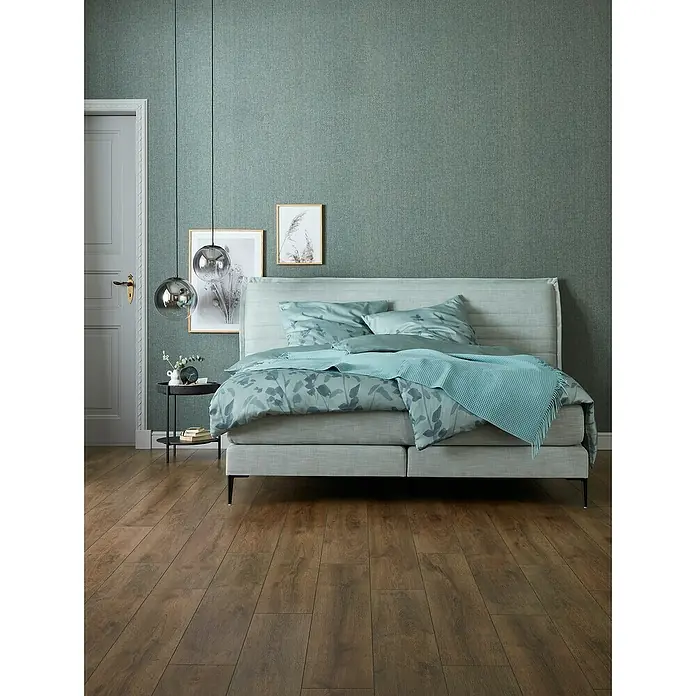 SCHÖNER WOHNEN-Kollektion Vliestapete Unistruktur - Grün/Grau, Uni, 10,05 x 0,53 m - Ein elegantes Schlafzimmer mit einem Boxspringbett in beruhigenden Blau- und Grautönen, ergänzt durch passende Nachttischlampen und Wanddekorationen.