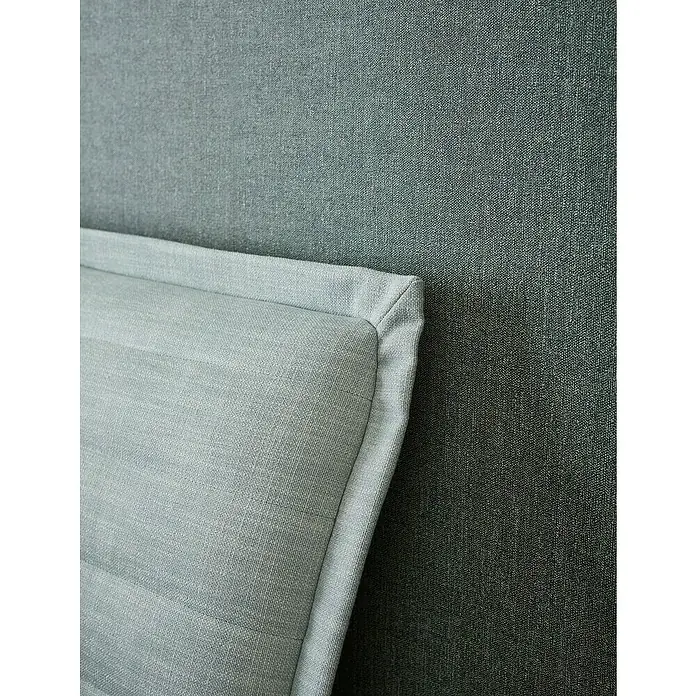 SCHÖNER WOHNEN-Kollektion Vliestapete Unistruktur - Grün/Grau, Uni, 10,05 x 0,53 m - Nahaufnahme einer eleganten, hellblauen Zierkissen-Ecke, die auf einem strukturierten, dunkleren Stoff liegt. Die Texturen kontrastieren schön.