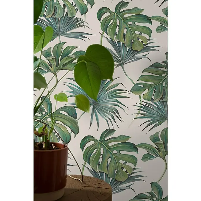 SCHÖNER WOHNEN-Kollektion New Spirit Vliestapete Fensterblatt - Grün/Weiß, Floral, 10,05 x 0,53 m - Zimmerpflanze in braunem Topf vor einer Tapete mit tropischen Blättern. Die Pflanze ist ein Blickfang im Raum.
