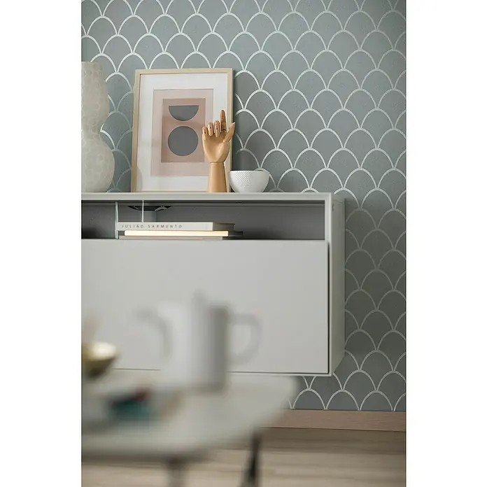 SCHÖNER WOHNEN-Kollektion New Spirit Vliestapete - Grün, Grafisch, 10,05 x 0,53 m - Nahaufnahme eines stilvollen Sideboards in Weiß mit Dekorationsgegenständen auf einer Oberfläche mit gemusterter Tapete.
